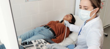 Female endocrinologist in whitecoat and mask sitting by ultrasound equipment