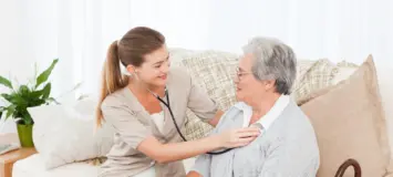a female professional home health aide is assisting an elderly patient in their home